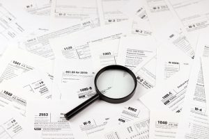 Magnifying glass lying over heap of paper documents. Investigation and financial audit