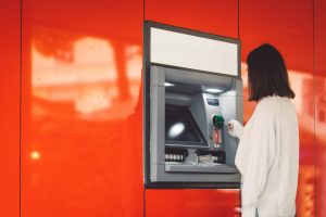 Side view of a woman inserting a card in the ATM on a red wall