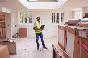 Builder Wearing Hard Hat With Clipboard Checking Delivery Of New Kitchen Units Inside Property
